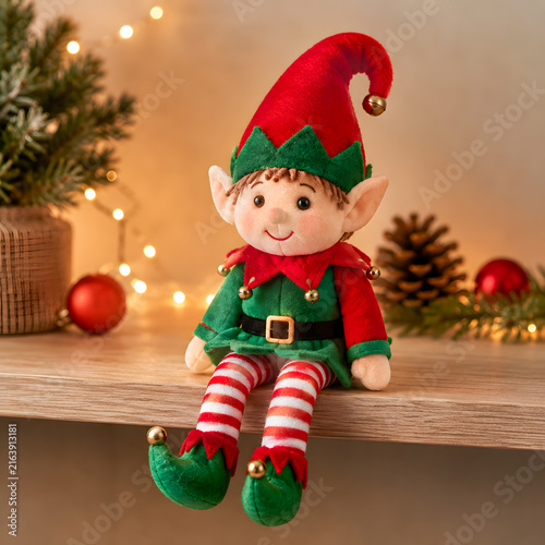 Plush Christmas elf doll sitting on a shelf with festive decorations  