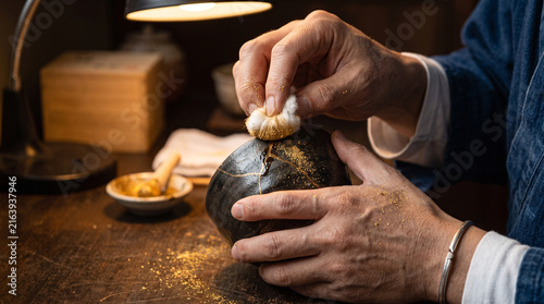 Artisan restorer applying gold dust to ceramic bowl using traditional kintsugi technique