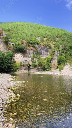 scenic stone village nestled in green mountain gorge along clear river, gorge of the Tarn in France, vertical video