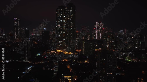 An aerial view of Mumbai's high-rise buildings and beautiful nightlights. The sky is cloudy, and there is medium traffic on the road. The cityscape is filled with modern illuminated buildings.