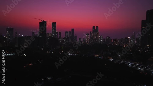 A breathtaking aerial drone view of the Mumbai skyline at sunset and blue hour, with modern skyscrapers lit against a vibrant orange-and-purple twilight sky.