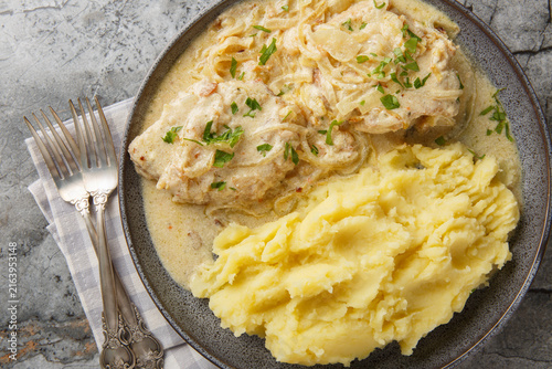 Juicy German schnitzel with onion cream sauce and served with mashed potatoes close-up in a plate on the table. Horizontal top view from above
