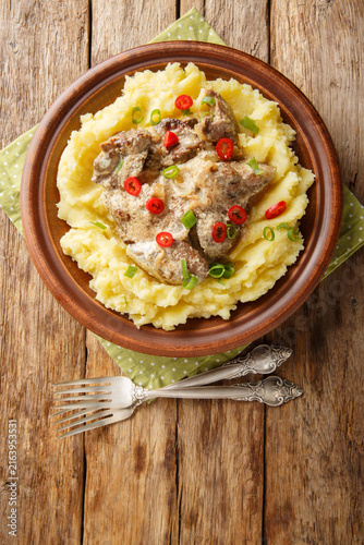 Fried liver with onions and sour cream served with mashed potatoes close-up in a plate on the table. Vertical top view from above