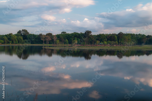 A pond with reflections of the clouds in the sky, with mountains in the background, in the evening.