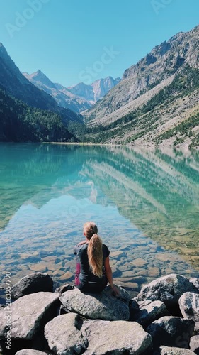 woman sitting on rocks looking at turquoise alpine lake reflection in mountain valley, Gaube lake in France