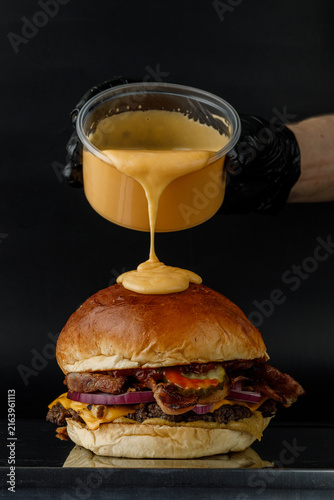 Obraz na plátně Pouring melted cheese on a gourmet bacon burger