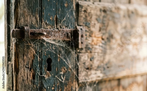 Old weathered wooden door with rusty latch and cobwebs representing abandonment and decay