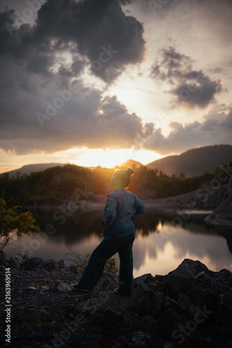 Obraz na plátne Vertical view of young woman standing against sunset sky reflected on peaceful mountain lake