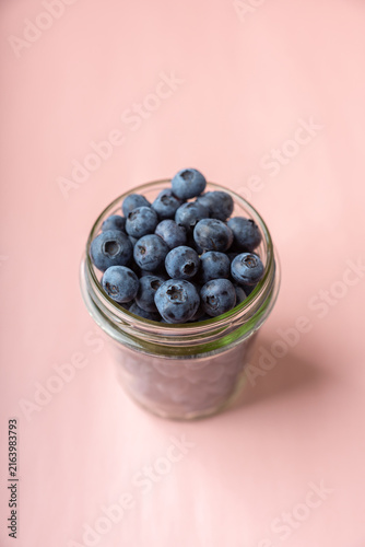 Принти на полотні Glass jar filled with blueberries on pastel pink background