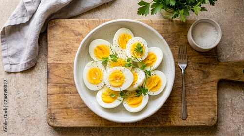 Quadro su tela Top-down view of sliced hard-boiled eggs with black pepper and microgreens in a bowl, placed on a wooden cutting board with a fork