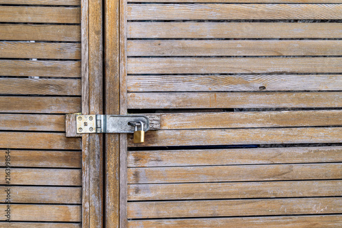 Vintage wooden slatted door locked with a brass padlock on a metal latch,A metaphor for mystery, locked secrets, inaccessible places or psychological barriers.