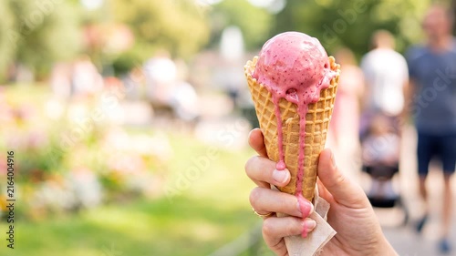 Hand holding pink ice cream cone in a sunny park setting  