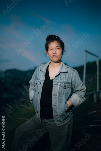 Fotografie Playful young woman winking at camera wearing denim jacket outdoors at twilight