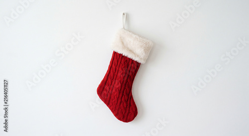 Single red knitted Christmas stocking with a white faux fur cuff hanging on a white background with copy space