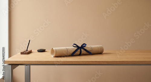 Architectural blueprint scroll tied with a navy blue ribbon on a wooden desk with a pen in a holder and a computer mouse