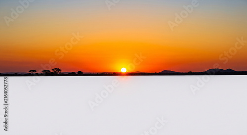 Vibrant orange and yellow sunset over a silhouetted landscape with trees and mountains creating a serene natural scene