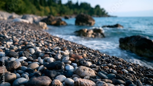A close up view of smooth pebbles on a rocky shoreline where gentle waves lap against the shore under soft natural light