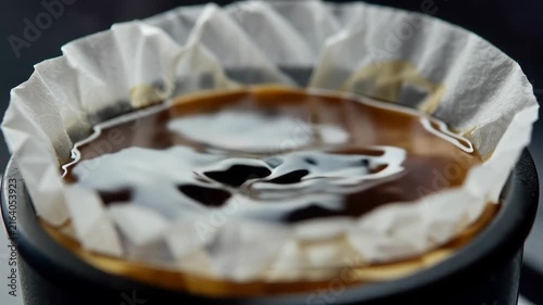 Water is poured into a coffee filter filled with ground coffee, creating a rich brew in a black cup, showcasing the brewing process in a kitchen setting