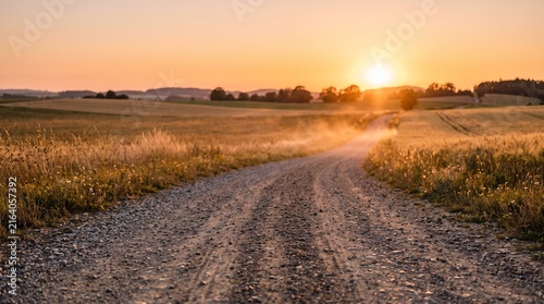 Dusty gravel road at sunset in rural countryside landscape with golden hour light