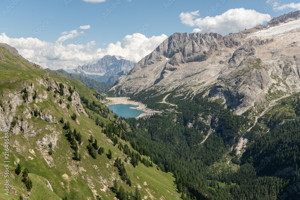 Obraz premium Arabba, Italy. Panoramic alpine landscape overlooking Lago di Fedaia reservoir, forested Dolomite valleys and the Marmolada mountain massif