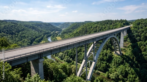 Concrete arch bridge crossing a lush green valley with a river flowing below in summer.