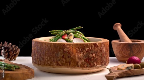 Gourmet green asparagus salad in rustic wooden bowl on white and black background