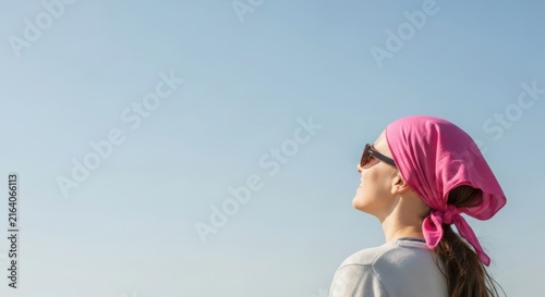 Young woman wearing a pink headscarf and sunglasses looking up at the clear blue sky