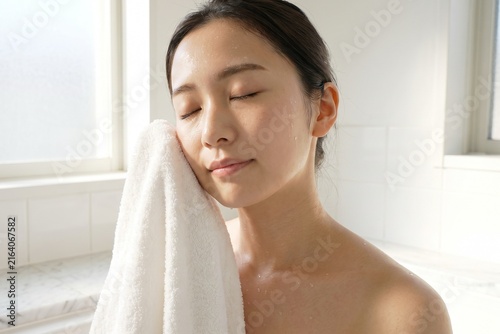 明るい洗面所で顔を拭く若い女性（ライフスタイル・健康・お風呂上がり・コピースペース）