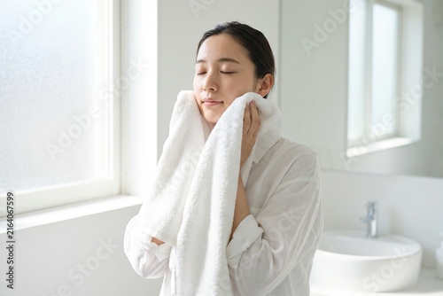 明るい洗面所で顔を拭く若い女性（ライフスタイル・健康・お風呂上がり・コピースペース）