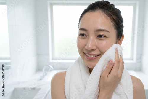 明るい洗面所で顔を拭く若い女性（ライフスタイル・健康・お風呂上がり・コピースペース）