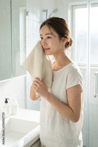 明るい洗面所で顔を拭く若い女性（ライフスタイル・健康・お風呂上がり・コピースペース）
