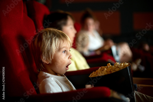 Cute child, boy, watching movie in a cinema, eating popcorn and enjoying