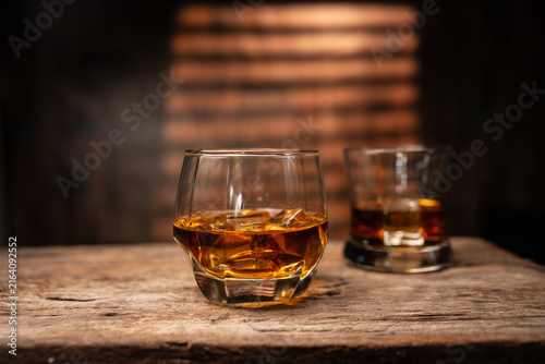 Whiskey Glass with Ice Cubes on Wooden Table in Bar