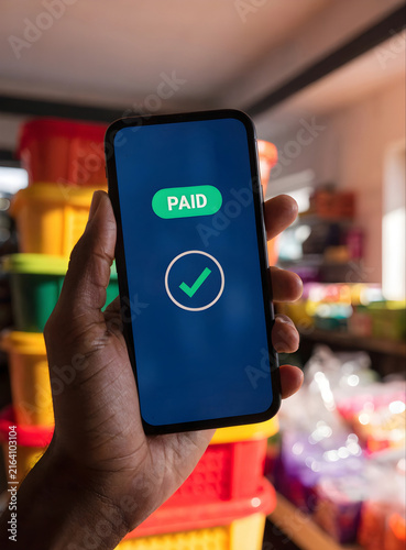 Hand Holding Smartphone Displaying Paid Confirmation Screen with Checkmark in Retail Store