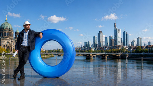 European Engineer Leaning Against a Blue O Ring Sculpture in a Modern City	