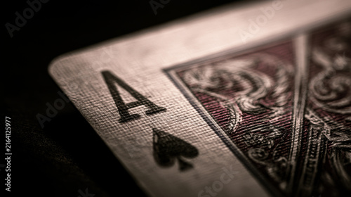 A close view of an ace of spades card is on a dark surface. The card shows detailed patterns and textures. This setting highlights the card's features and design