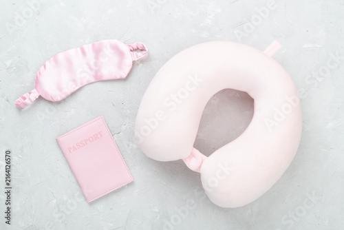 Pink travel pillow with sleeping mask and passport on concrete background, top view