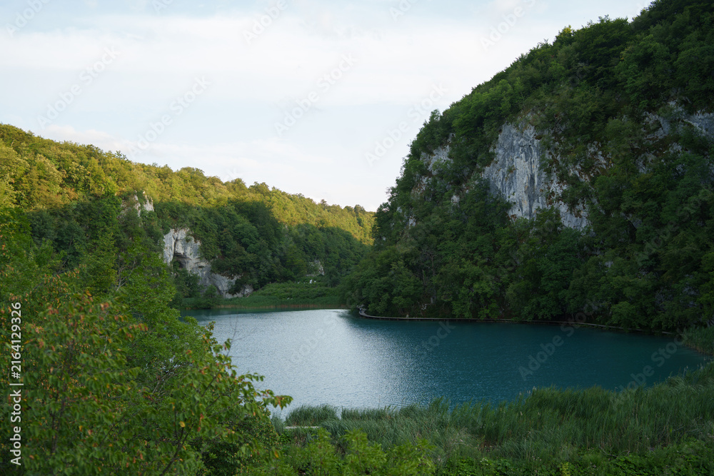 Fototapeta premium Crystal clear turquoise lake surrounded by lush forest in Plitvice Lakes National Park, showcasing pristine natural water and scenery.