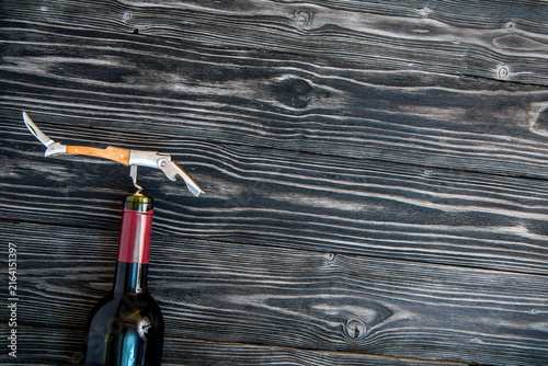 glass wine bottle and corkscrew on wooden background top view