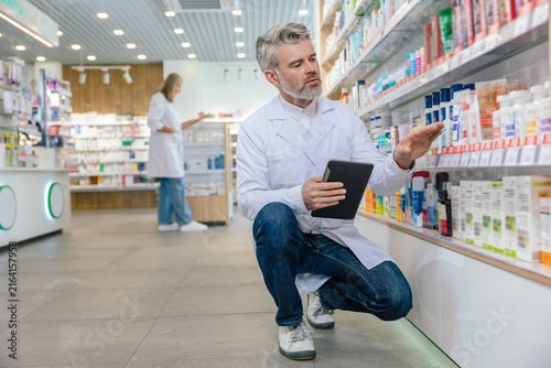 Canvastavla Male pharmacist with a tablet in hands revising medicines on the shelves in a ph