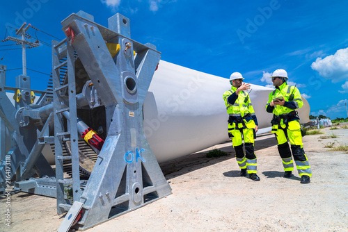 Фотография Two wind farm engineers face each other in conversation beside a huge stored tur