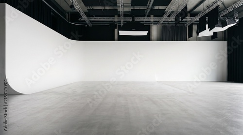 A spacious professional photo and film studio with a white cyclorama wall, polished concrete floor, and ceiling-mounted lighting equipment.