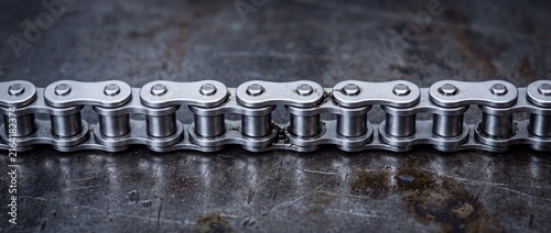 Industrial steel roller chain for power transmission machinery lying horizontally on dark scratched metal surface in manufacturing workshop