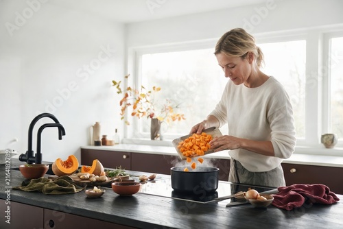 Woman cooking pumpkin soup with fresh vegetables in a bright autumn kitchen
