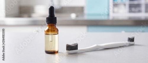 Amber glass dropper bottle with transparent liquid stands next to white double-sided toothbrush on sterile countertop