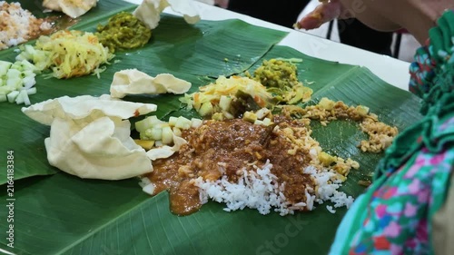 Closeup of hand and finger mixing rice with curry served on banana leaf, popular Indian food in restaurant in Malaysia. Eating with hand is culturally common within the Indian community.