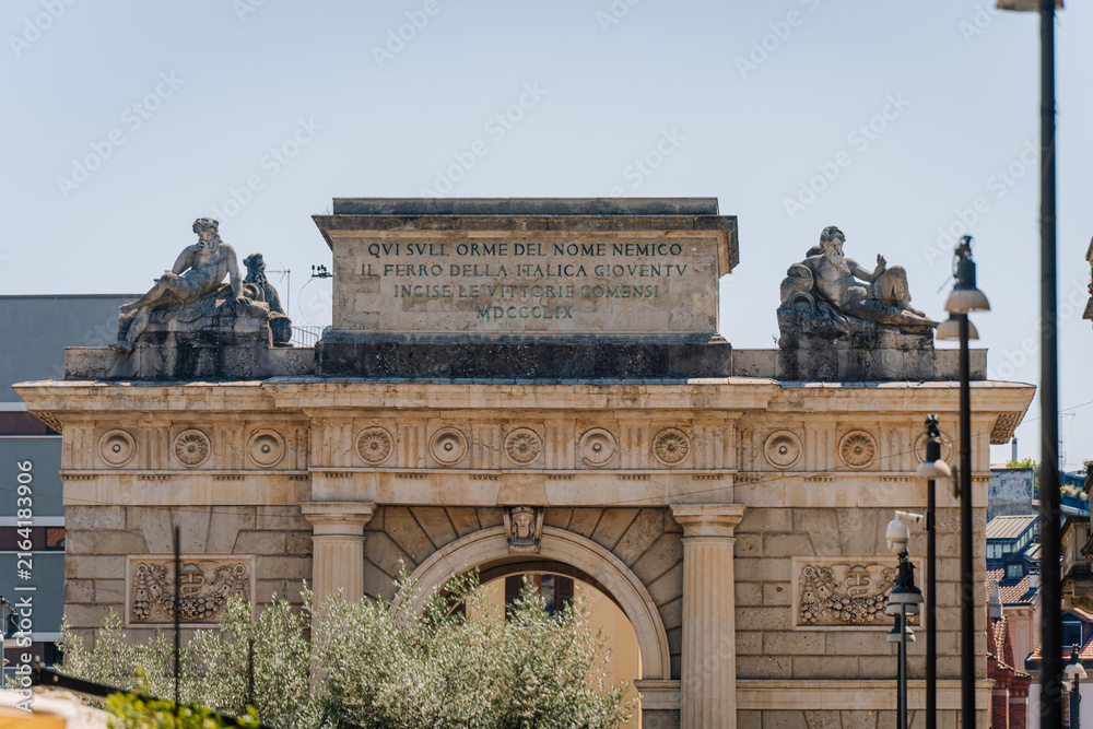 Fototapeta premium Historical arch monument with sculptures and inscriptions in Milan, showcasing classical architecture and decorative elements in a public square