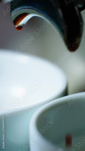 An espresso machine releases rich dark coffee that drips slowly into two waiting white cups. The setting is warm and inviting, perfect for a morning pick-me-up.