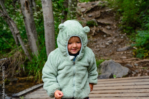 Three-year-old girl standing on a wooden bridge in a green forest