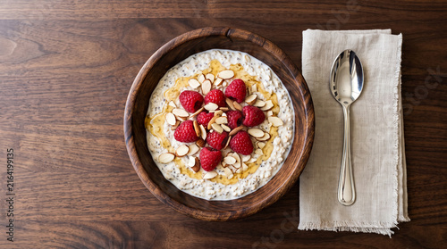 Top Down Flat Lay View of Healthy Overnight Oatmeal Bowl Topped with Fresh Raspberries Sliced Almonds and Honey Drizzle on Rich Wooden Table with Copy Space